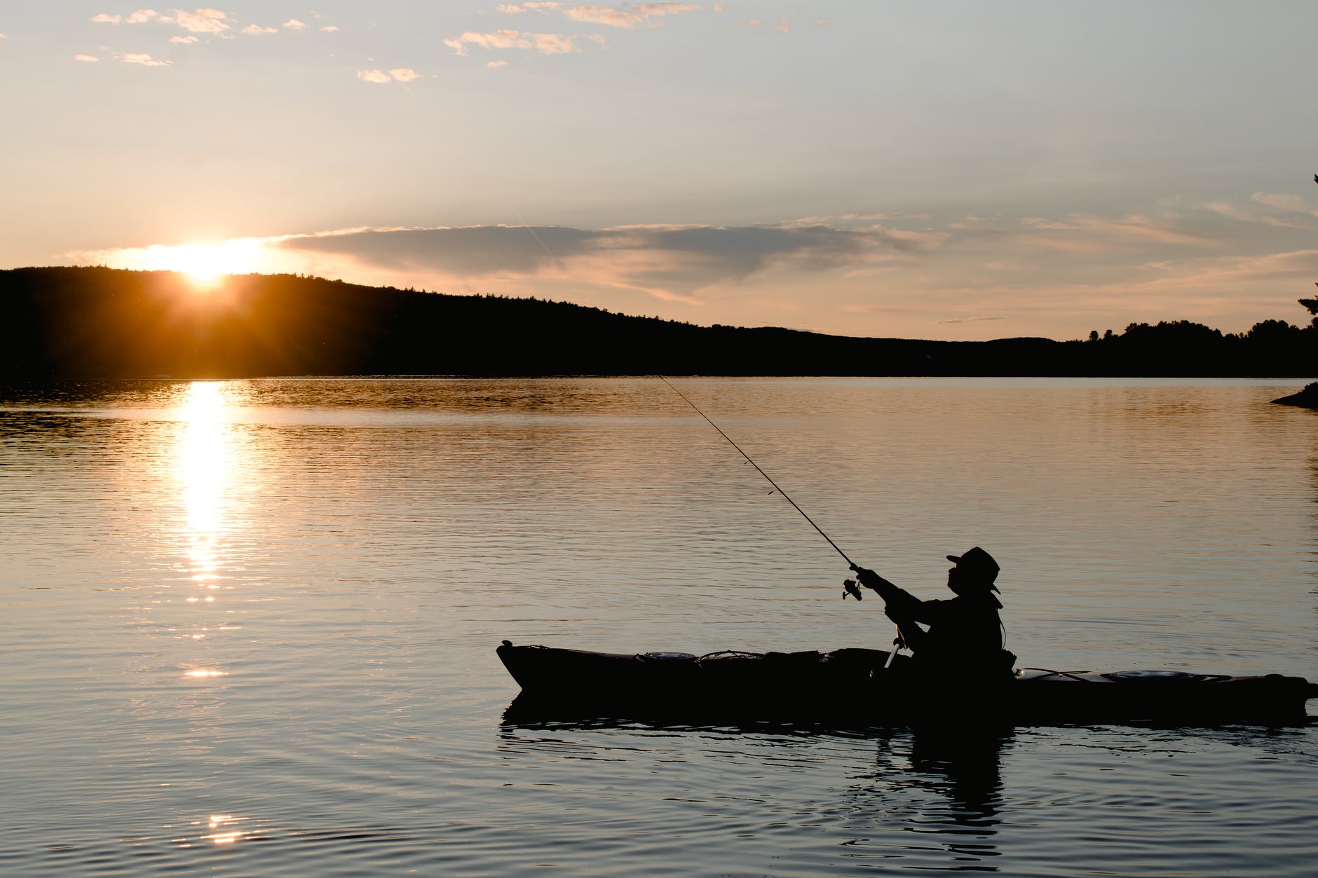unrecognizable fisherman in boat fishing on lake at sunset
